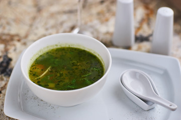 Minestrone soup with arugula served in a white bowl with ceramic spoon, glass of white wine on marble table