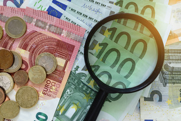 Magnifying glass on pile of Euro banknotes with Euro coins as financial analysis concept.