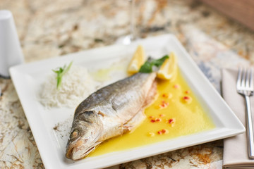 Whole boiled wolffish served with sauce from lemon butter and white wine on square white plate