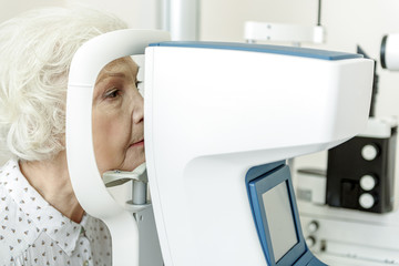 Serious old woman sitting near optical apparatus