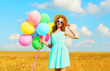Happy smiling young woman with an air colorful balloons enjoying a summer day on a field blue sky background