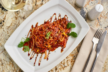 Spicy tofu served on white plate with glass of white wine on marble table. Vegeterian cuisine.