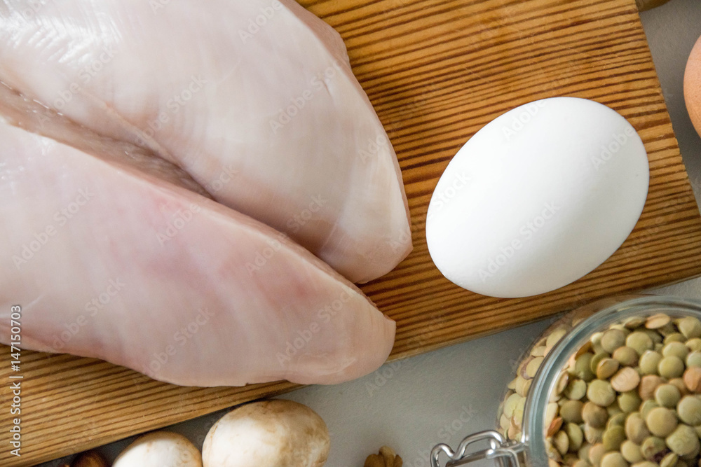 Wall mural raw food grocery full of proteins on wooden brown cutting rustic board on white table. chicken fille