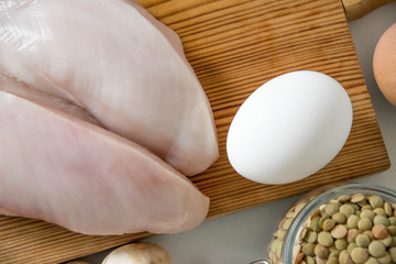 Raw food grocery full of proteins on wooden brown cutting rustic board on white table. Chicken fillet, eggs, mushrooms, lentils. Healthy sport diet background. Healthcare lifestyle or proteins concept