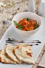 Chicken fillet slices fried in spicy cream sauce with tortilla bread served in white bowl with glass of wine, knife and fork on napkin on marble table