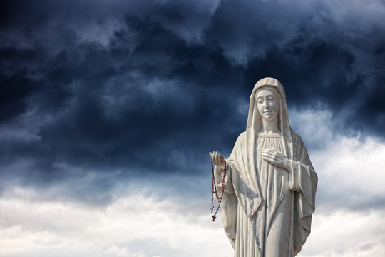 A statue of the Virgin Mary against a dramatic sky.