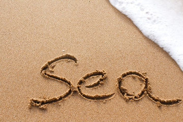 Fototapeta na wymiar Sea word handwritten on the sand with wave on background