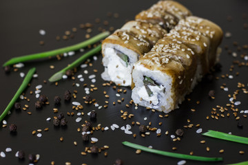 Eel sushi rolls with sesame seeds on black background 