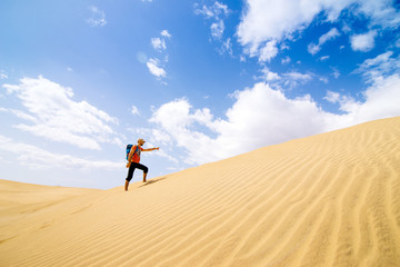 A tourist with a backpack shows the direction of movement in the desert on a background of blue sky