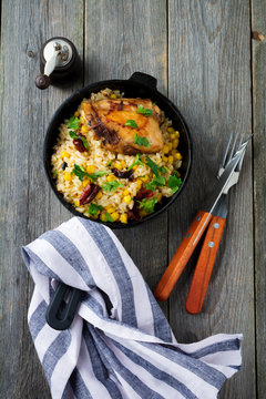 Rice with corn, soy sauce and fried chicken thigh on a cast-iron frying pan. Top view. Selective focus.