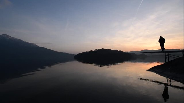 A man catches a fish. Happy relaxed hours alone with nature. Landscape of a mountain lake. Evening light of the setting sun. Animation camera movement.