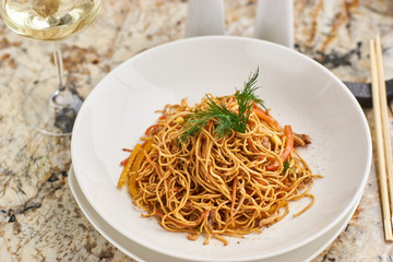 Flat egg noodles with pork slices served on white plate with white garlic and red spicy sauce