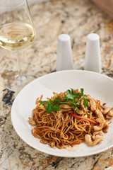 Thin egg noodles with chicken slices served on white plate with white garlic and red spicy sauce