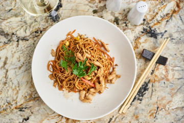 Thin egg noodles with chicken slices served on white plate with white garlic and red spicy sauce