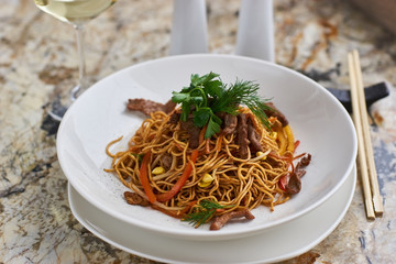 Thin egg noodles with beef meat slices served on white plate with white garlic and red spicy sauce