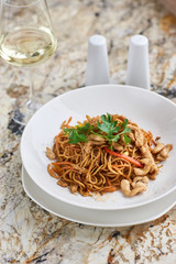 Thin egg noodles with chicken slices served on white plate with white garlic and red spicy sauce