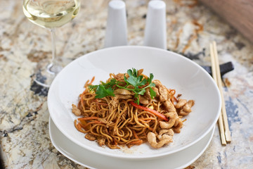 Thin egg noodles with chicken slices served on white plate with white garlic and red spicy sauce