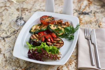 Grilled vegetables served on white plate. Eggplant, tomato, paprika and Zucchini slices.
