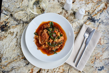 Vegetables tempura in sweet and sour sauce served in white round plate with glass of white wine on marble table