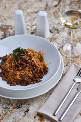 Fried rice with beef slices served in white round plate with glass of white wine on marble table