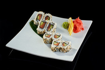 Sushi roll with fresh salmon and cucumber with vasabi, pickled ginger and lemon slice on white plate on black background