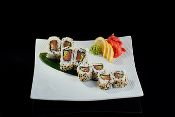 Sushi roll with fresh salmon and cucumber with vasabi, pickled ginger and lemon slice on white plate on black background