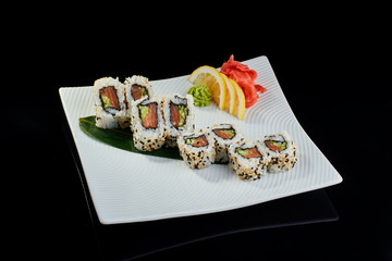 Sushi roll with fresh salmon and cucumber with vasabi, pickled ginger and lemon slice on white plate on black background
