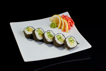 Vegeterian sushi roll with avocado with vasabi, pickled ginger and lemon slice on white plate on black background