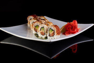 Sushi Roll with spicy eel fish, avocado and Philadelphia cheese with vasabi, pickled ginger and lemon slice on white plate on black background
