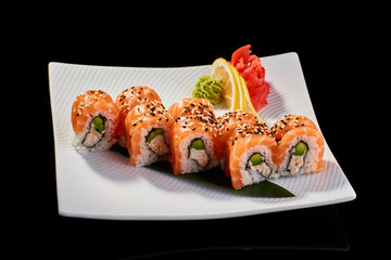 Sushi Roll with salmon and avocado served with vasabi, pickled ginger and lemon slice on white plate on black background
