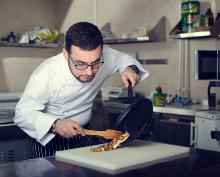 Chef Of The Restaurant Prepares An Omelette In A Frying Pan On The Stove In The Kitchen. Filtered Foto.