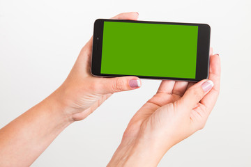 Closeup of young caucasian female hands holding modern smartphone with green touch screen isolated on white background. Horizontal color photo.