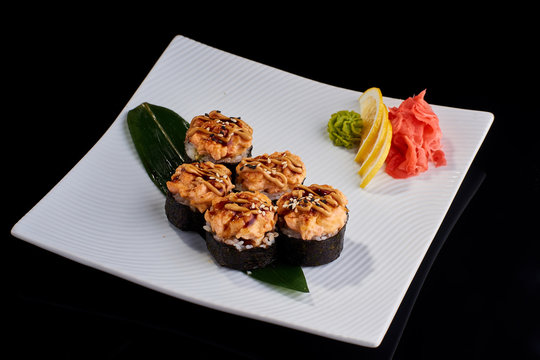 Baked Sushi Roll with crab, eel fish and spicy salmon served with vasabi, pickled ginger and lemon slice on white plate on black background