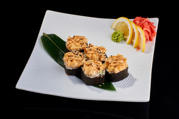 Baked Sushi Roll with perch, salmon and spicy scallops served with vasabi, pickled ginger and lemon slice on white plate on black background