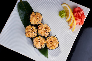 Baked Sushi Roll with perch, salmon and spicy scallops served with vasabi, pickled ginger and lemon slice on white plate on black background