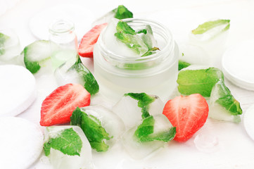 Refreshing summer homemade skincare. Cosmetic jar of hydrating ice cubes freezed with mint herb and fresh strawberry. Bright light botanical beauty treatment. 