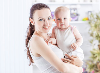 portrait of a happy mother with a year-old baby in her arms on the background of a child's room
