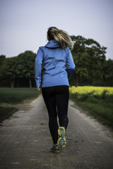 Sportliche junge Frau beim Jogging in den Feldern im Frühling