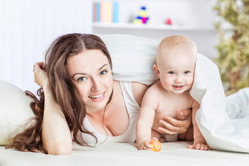 concept of happy mothers: happy mother and her year-old child playing on the sofa in the bedroom