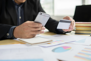 Man holding business card and dialing number at wooden desk,verifies account balance on mobile banking application.Online payment shopping,selective focus,vintage color