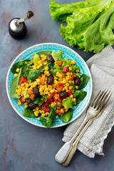  Warm salad with corn, pepper, olives and lettuce on a blue ceramic plate on a dark background. Selective focus.Top view.