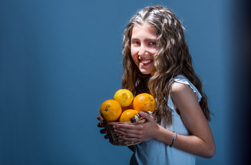 Fototapeta na wymiar Young girl holds a basket of fruit on a dark background