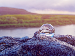 Magic glass ball on old stones. In the background is a river, a spring forest and a cloudy sky