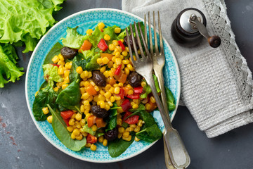  Warm salad with corn, pepper, olives and lettuce on a blue ceramic plate on a dark background. Selective focus.Top view.
