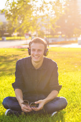 Naklejka na ściany i meble Handsome male student sitting on a green grass and listening music