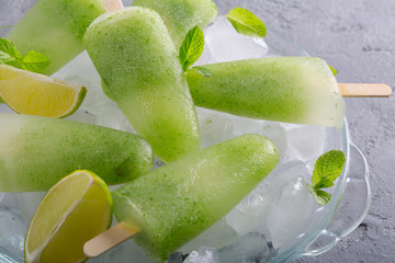 Homemade lime and mint leaves popsicles piled up on a plate of ice on grey concrete background. Side view