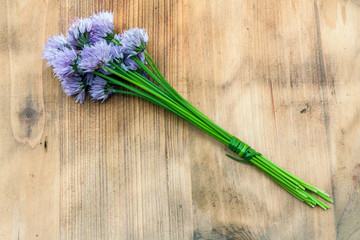 Flower chives tied in a snop on a natural wooden cutting board - obrazy, fototapety, plakaty