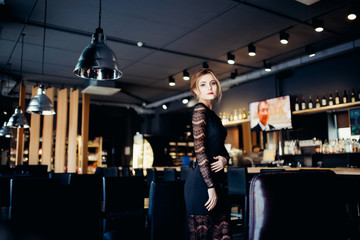 European-looking girl in a black evening dress at the restaurant welcomes guests.