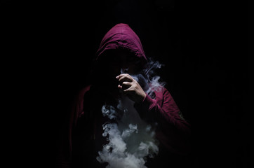 Vaping man holding a mod. A cloud of vapor. Black background. Vaping an electronic cigarette with a lot of smoke.