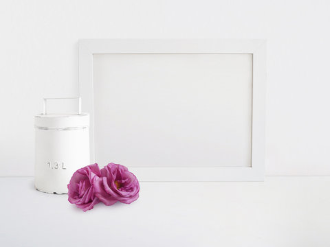 White blank wooden frame mockup with old tin and pink rose flowers lying on the table. Poster product design. Styled stock feminine photography. Home decor.